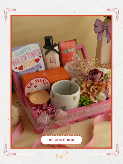 The 'Be Mine Box' is a classic romantic gesture. This pink wooden tray is filled with a heart-themed mug, a scented candle, skincare products, and a 'Be Mine' tag, making your intentions clear.