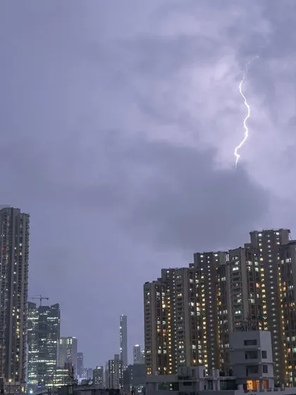 A single, bright lightning strike is captured in the cloudy night sky over Mumbai.