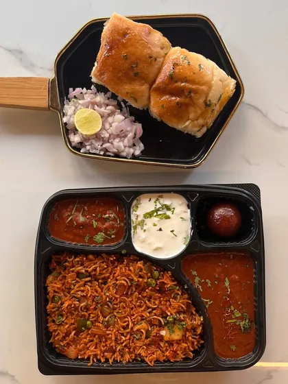 A taste of Mumbai in a box. This meal features spicy tawa pulao with a side of pav bhaji, raita, and a gulab jamun, accompanied by buttered pavs. It's a favorite for casual gatherings and parties.