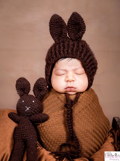 This little one is ready for a nap in a cute, hand-knitted bunny outfit, complete with long ears. The matching toy bunny adds an extra touch of charm.