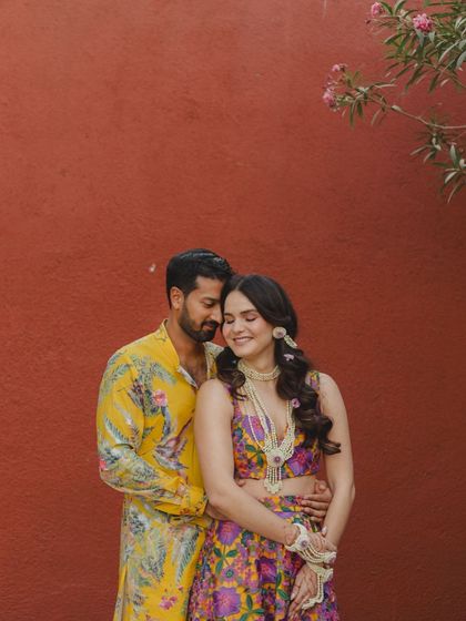 A sweet embrace against a bold red wall. The contrast of their colorful floral outfits and the solid background makes this a striking and intimate portrait from their Haldi ceremony.