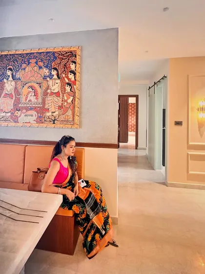 A shot of me sitting in a dining nook with a large Pattachitra painting on the wall, demonstrating how art is integrated into daily life.