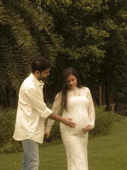 A tender moment between the expecting parents. The father-to-be gently touches the baby bump, a simple gesture full of love and connection, captured in a natural outdoor setting.