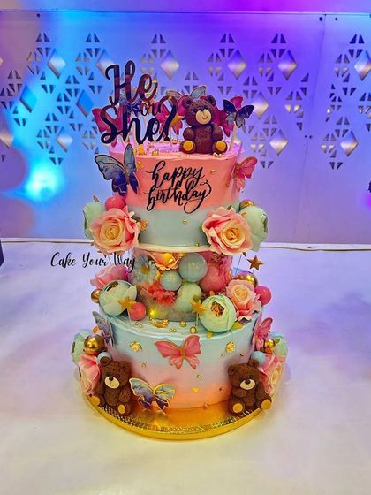 A grand three-tier cake for a combined birthday and baby shower celebration, with teddy bears, butterflies, and flowers.
