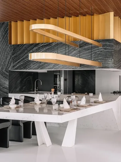 For the Tellado Villas, the goal was to create a confluence of social spaces. This open-plan dining and kitchen area uses bold forms, like the sculptural dining island and dramatic black marble, contrasted with the warmth of a wooden ceiling. It is a space designed for gathering, conversation, and shared experiences.