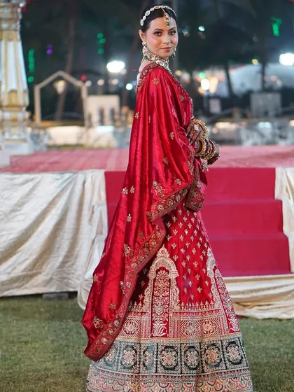 A full-length shot of the bride, showcasing her magnificent red and green lehenga with intricate embroidery.