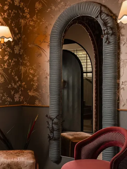 The pleated mirror in its full context. Framed by floral wallpaper and flanked by soft wall sconces, its unique fabric-wrapped frame becomes a central art piece, reflecting the room's romantic and layered aesthetic.