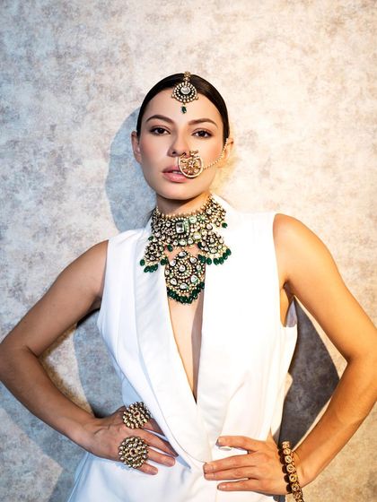 A bold, high-fashion look. The traditional nath, maang tikka, and choker are styled with a contemporary white vest.