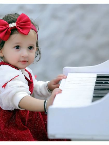 A close-up of a little girl playing the piano, dressed in a beautiful red outfit. Our prop setups are perfect for creating classic portraits.