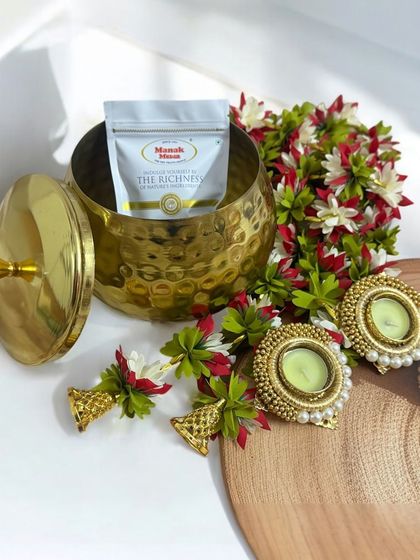 Here's another view of the popular metal handi hamper, showing the contents more clearly. It includes a packet of premium dry fruits, festive door hangings, and pearl-studded T-light holders, making it a wonderful household gift.