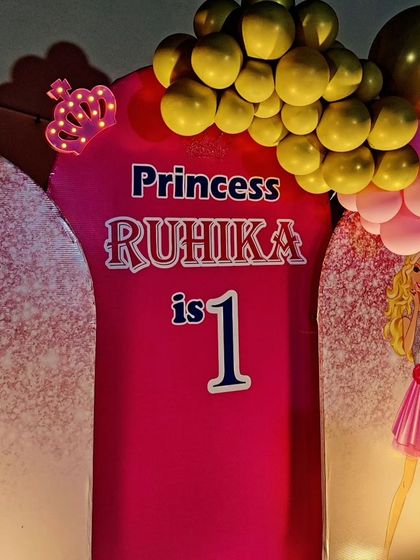A close-up of a princess-themed first birthday backdrop, featuring Barbie and a crown detail.