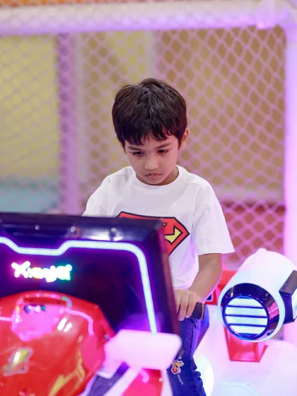Dressed as Superman, this little hero is focused on his mission at the arcade game station during a fun-filled birthday party.