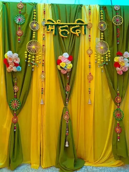 A creative Mehndi backdrop combining yellow and green drapes with unique, handcrafted hangings and floral bunches. This decor is perfect for adding a touch of personalized, folksy charm to your event.