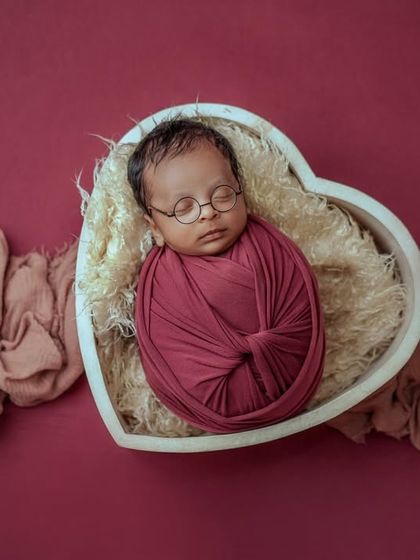 A sleepy little scholar. Even in their dreams, this baby looks ready to learn, nestled in a heart-shaped basket with their tiny glasses.