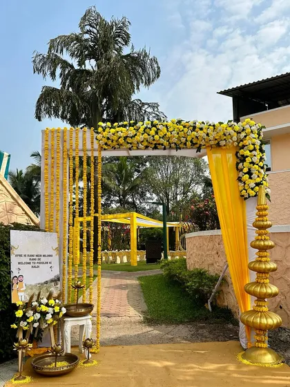 The entrance to a 'Phoolon ki Haldi' event, decorated with yellow drapes, marigold garlands, and a welcoming sign for the guests.