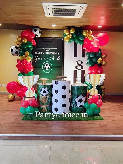 A football-themed birthday party perfect for a young sports fan. The setup includes a goalpost backdrop, trophy props, football-themed pedestals, and balloons in team colors.