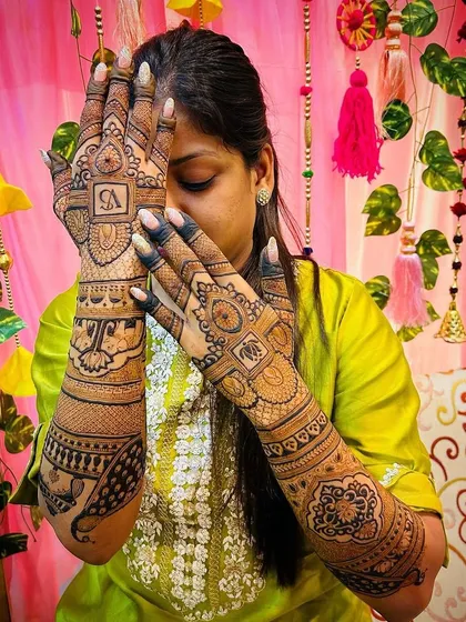 A happy bride showing off her full-arm mehndi with a mix of initial monograms and traditional patterns.