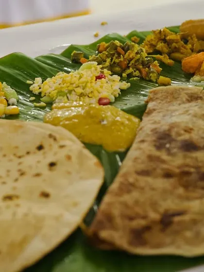 The heart of South Indian celebrations is the 'Yele Oota'. This close-up shows a traditional meal served on a banana leaf, featuring a variety of dishes like roti, sabzi, and dal, all prepared authentically.