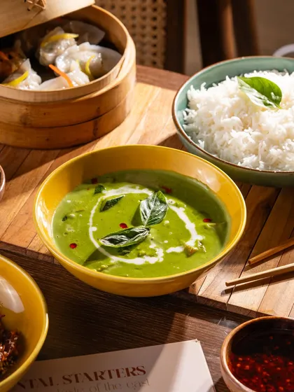 A vibrant Thai green curry. The swirl of coconut cream and fresh basil leaves on top add visual appeal and signal freshness.