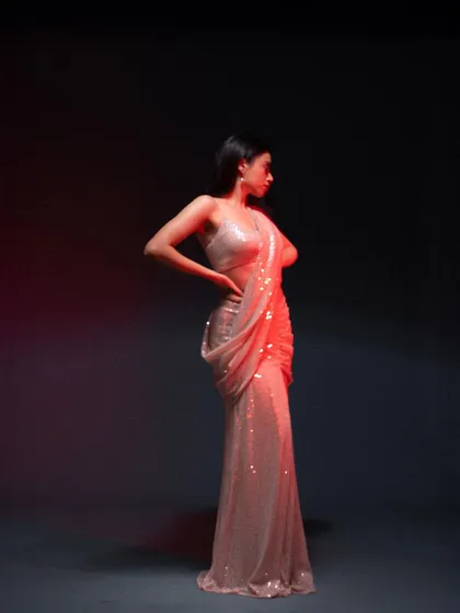 A full-length shot of a sequined saree, using dramatic lighting to highlight its sparkle. The dark background and red light accents create a glamorous and modern feel.