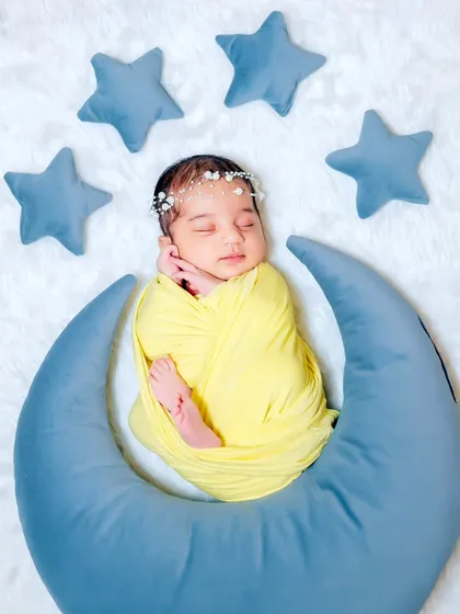 A top-down view of a newborn sleeping on a moon pillow, surrounded by soft blue stars. This celestial theme is perfect for your little star.