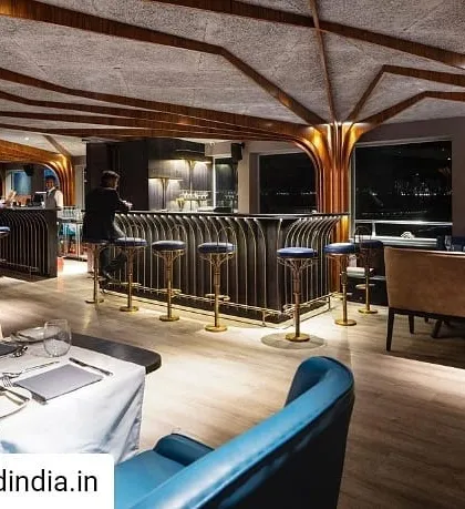 The restaurant's interior bar and lounge area at night. The warm lighting highlights the texture of the wood-paneled walls and the intricate details of the brass bar stools, creating an inviting ambiance for evening dining.
