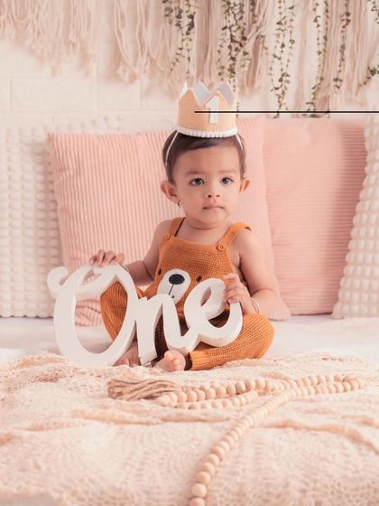 A sweet portrait of this little one celebrating his first birthday. The bear-themed outfit and the "ONE" sign create a cohesive and adorable milestone photo.