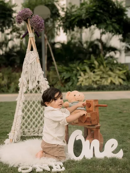 Celebrating a first birthday outdoors with a teepee, teddy bear, and wooden props for a rustic, natural feel.