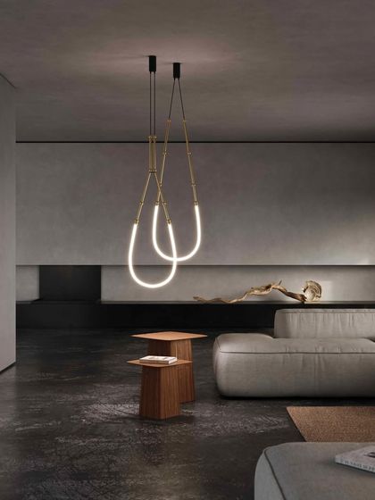 The Leda flexible lighting system by Karman is arranged in graceful, looping forms in a minimalist living room. The glowing silicone tubes, reminiscent of precious jewels, add a soft, sculptural element to the stark, modern space.