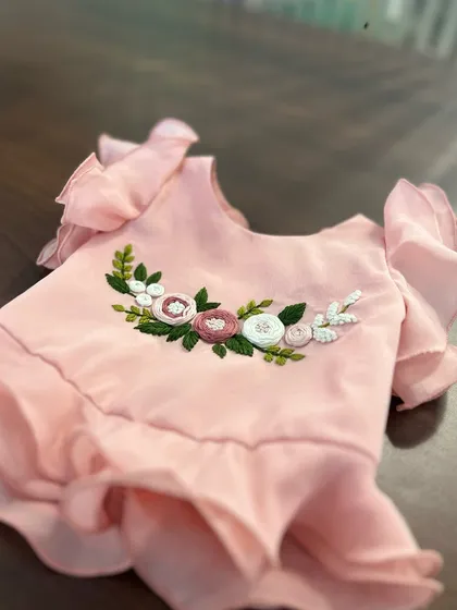 A full view of the hand-embroidered floral detail on a ruffled top for kids.