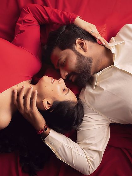 An artistic, top-down shot capturing an intimate gaze between the couple. The rich red fabric creates a beautiful canvas of love.