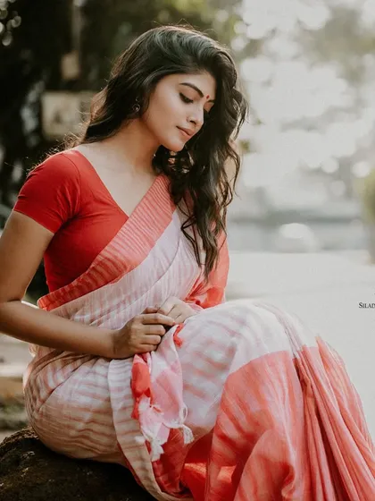 A serene, seated portrait of a model in a red and white saree. The soft, natural light and her contemplative pose create a peaceful and timeless image.