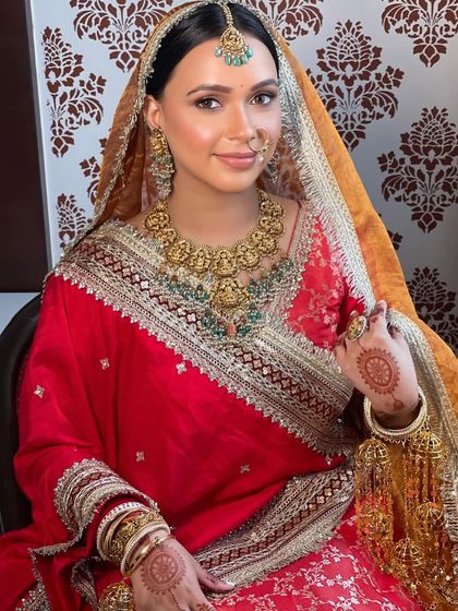 A royal bride in red and gold. Her hair is styled in a clean, elegant bun to complement her majestic look.