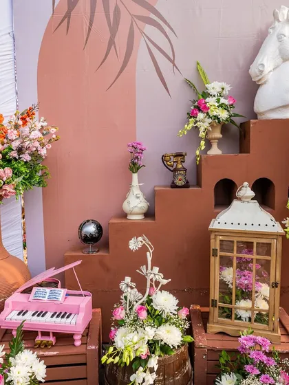 A close-up of the whimsical decor details at the carnival, including a miniature pink piano, a horse-head statue, and various floral arrangements.