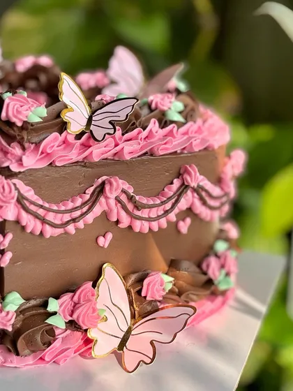 A detail shot of the chocolate vintage cake, focusing on the layers of piped buttercream, tiny hearts, and the delicate, gold-trimmed butterfly accents.