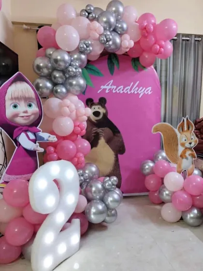 A classic Masha and the Bear theme for Aradhya's second birthday. The setup includes large character cutouts, a light-up number two, and a pink and silver balloon garland to complete the look.