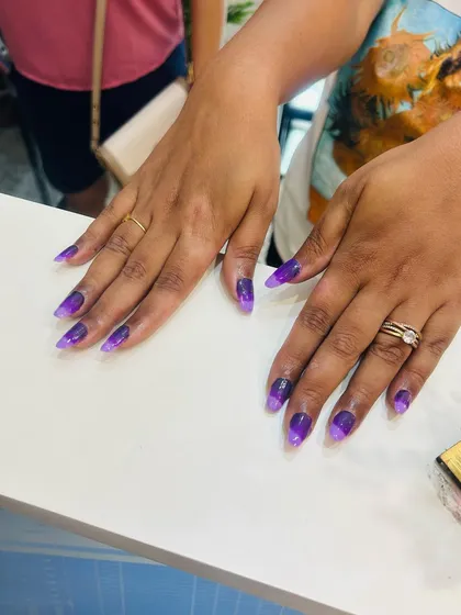A full set of sharp, stiletto-shaped nail extensions featuring a purple ombre effect. The color fades from a deep violet to a lighter lavender, creating a moody and stylish look.
