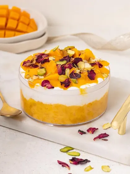 A beautiful mango dessert tub garnished with rose petals and pistachios. This fusion of flavours is highlighted by the elegant styling with a golden spoon and ribbon.