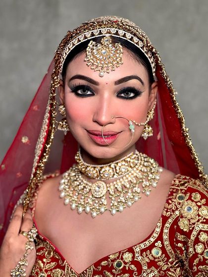 A smiling bride, radiating happiness in our classic red bridal lehenga. The pearl-drop kundan necklace is a perfect match.