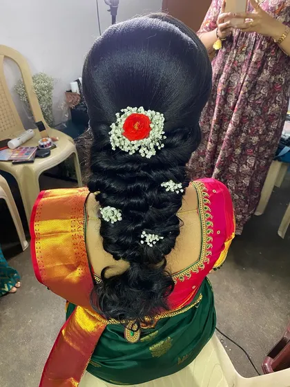 A beautiful messy braid adorned with baby's breath and a central red flower. This is a romantic and elegant hairstyle, perfect for an engagement or reception.