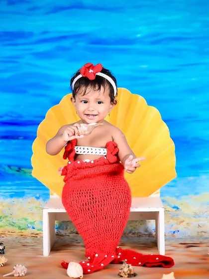 A happy baby girl dressed as a mermaid, sitting on a seashell by the "sea."