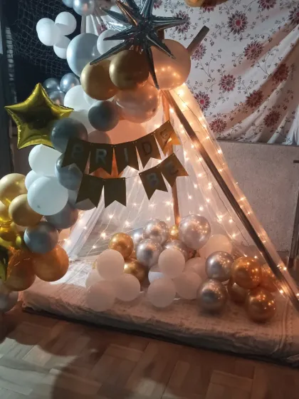 A cabana tent decoration on a terrace or balcony. This setup for a "Bride to Be" uses gold, silver, and white balloons and fairy lights to create a cozy and celebratory nook.