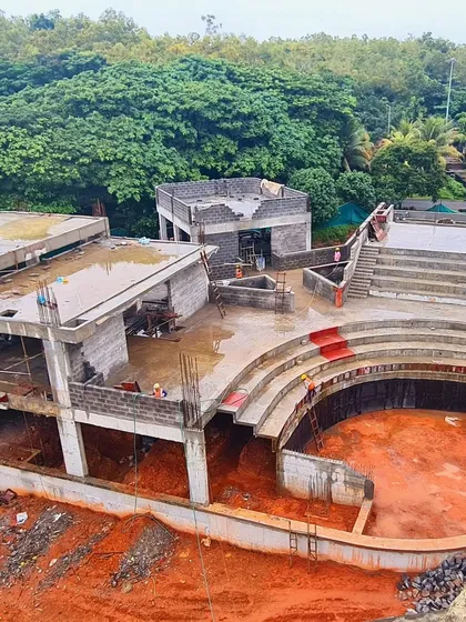 An aerial view of the TAPMI Centre's concrete structure during construction, highlighting the building's footprint and its relationship to the surrounding green campus.