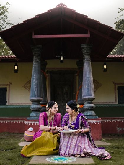 Two women in traditional dress sitting in front of a classic South Indian home, capturing the essence of cultural heritage.
