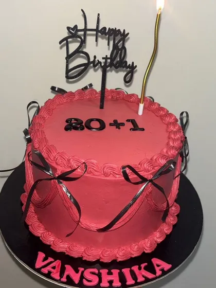 A fun and chic cake for a 21st birthday. The vibrant pink frosting is accented with black ribbons for a modern, gift-wrapped look, celebrating a special milestone with a touch of playful elegance.