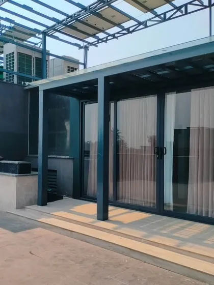 The exterior of a modern, dark-themed terrace room with large sliding glass doors. This structure is designed to house an office or studio space.