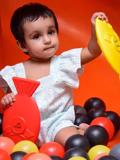 A toddler discovers the fun of our ball pit, finding colorful toy fish among the balls. It's a gentle and engaging space for our youngest guests.