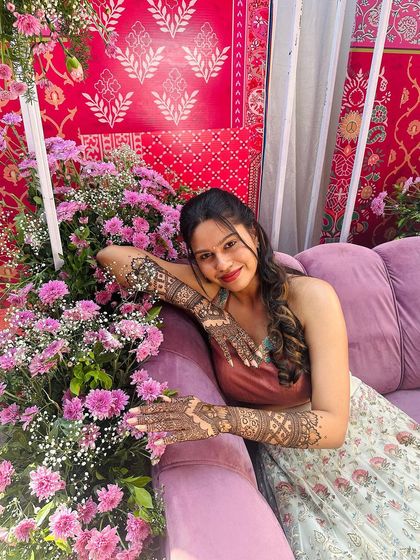 A happy bride posing on a purple sofa surrounded by flowers.