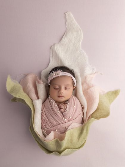 Like a precious pearl in a shell, this baby girl is swaddled in pink and resting inside a beautiful, artistic flower prop. The pearl details on her wrap add a touch of luxury.