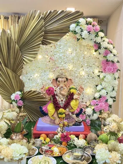 This modern Ganpati decor combines traditional flowers with contemporary elements. A beautiful crescent of white and pink flowers is accented with large, golden dried palm leaves, creating a stylish and sophisticated look for the festival.